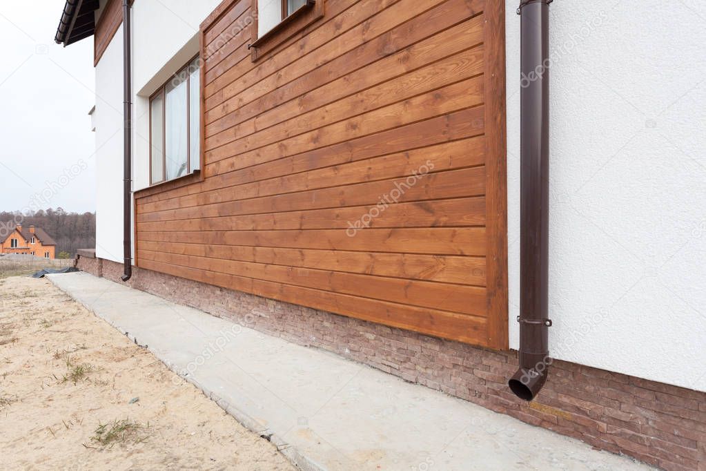 New brown copper gutter in house with white wall and wooden planks.