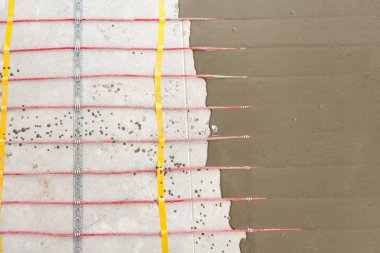 Elektrikli yerden ısıtma sistemi yüklemesi yeni evde. Beton ve kırmızı elektrik telleri closeup.