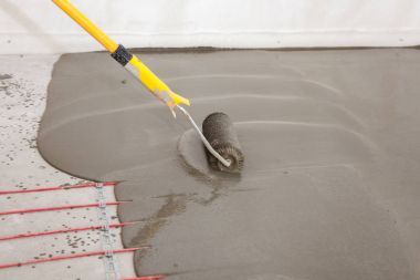 Elektrikli yerden ısıtma sistemi yüklemesi yeni evde. İşçi çimento ile silindir hizalama.