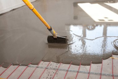 Elektrikli yerden ısıtma sistemi yüklemesi yeni evde. İşçi çimento ile silindir hizalama.