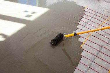 Elektrikli yerden ısıtma sistemi yüklemesi yeni evde. İşçi çimento ile silindir hizalama.