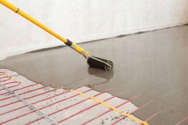 Elektrikli yerden ısıtma sistemi yüklemesi yeni evde. İşçi çimento ile silindir hizalama.