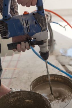 Elektrikli yerden ısıtma sistemi yüklemesi yeni evde. İşçi çimento hazırlamak için beton el mikseri kullanın.