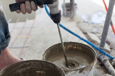 Elektrikli yerden ısıtma sistemi yüklemesi yeni evde. İşçi çimento hazırlamak için beton el mikseri kullanın.