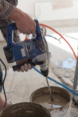 Elektrikli yerden ısıtma sistemi yüklemesi yeni evde. İşçi çimento hazırlamak için beton el mikseri kullanın.
