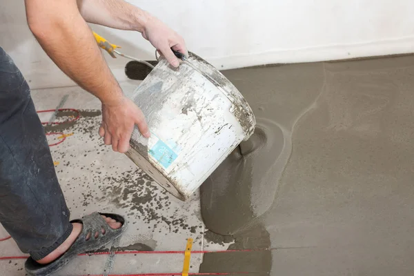 Electric floor heating system installation in new house. Worker pouring concrete on the floor.