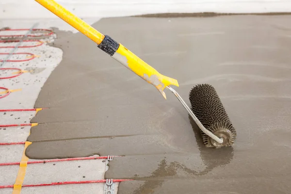 Electric floor heating system installation in new house. Worker align cement with roller. — Stock Photo, Image