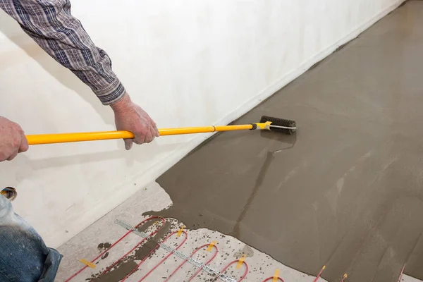 Electric floor heating system installation in new house. Worker align cement with roller.