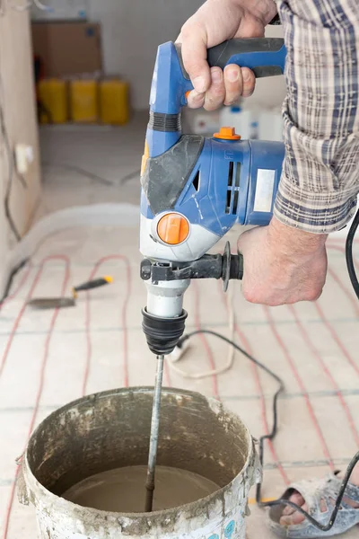 Installation einer elektrischen Fußbodenheizung im neuen Haus. Arbeiter verwenden Betonmixer, um Zement vorzubereiten. — Stockfoto