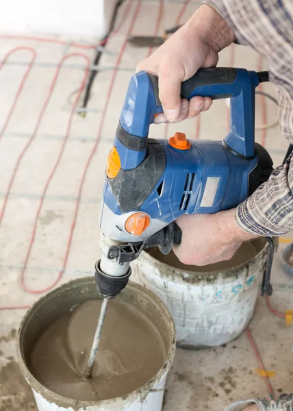 Elektrické podlahové vytápění instalace systému v novém domě. Pracovník použít konkrétní ruční mixér k přípravě cementu. — Stock fotografie