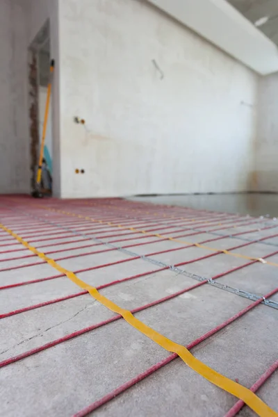 Electric floor heating system installation in new house. Closeup of concrete and red electrical wires.