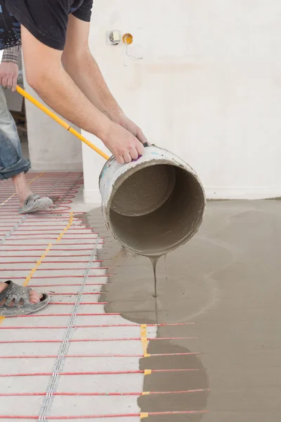 Electric floor heating system installation in new house. Worker pouring concrete on the floor.