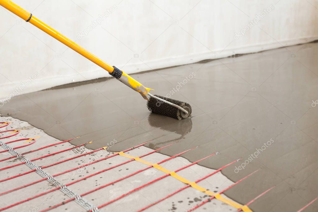 Electric floor heating system installation in new house. Worker align cement with roller.