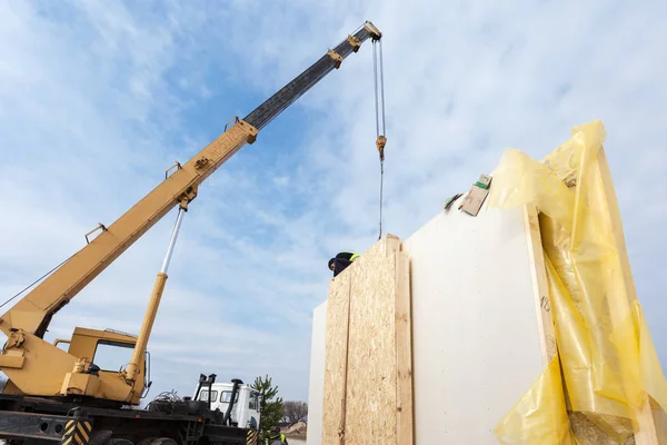 Руфер-строитель с краном, устанавливающий конструктивные страховочные панели СИП. Строительство нового дома с энергоэффективными рамами — стоковое фото