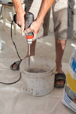 Elektrikli yerden ısıtma sistemi yüklemesi yeni evde. İşçi çimento hazırlamak için beton el mikseri kullanın