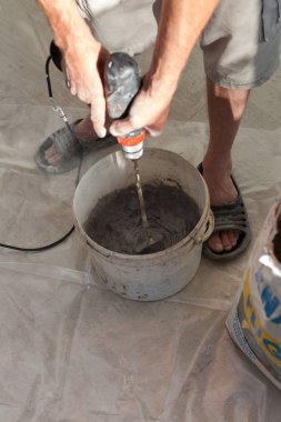 Elektrikli yerden ısıtma sistemi yüklemesi yeni evde. İşçi çimento hazırlamak için beton el mikseri kullanın.