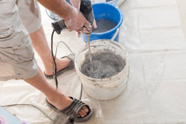 Elektrikli yerden ısıtma sistemi yüklemesi yeni evde. İşçi çimento hazırlamak için beton el mikseri kullanın.