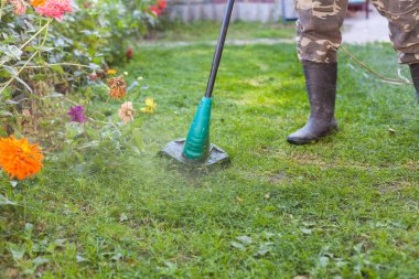 Lastik çizmeler önünde arka bahçesinde bir biçme makinesi ile adam