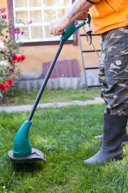 Lastik çizmeler önünde arka bahçesinde bir biçme makinesi ile adam