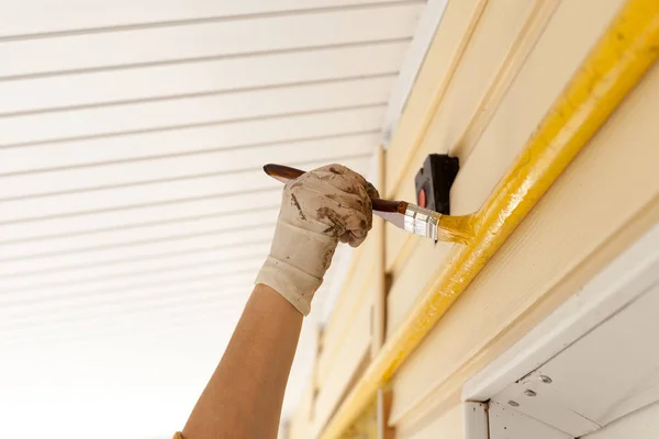 Arbeiter mit Handschuhen färben das Metallgasrohr mit gelber Farbe mit einem Pinsel mit Holzgriff ein. — Stockfoto