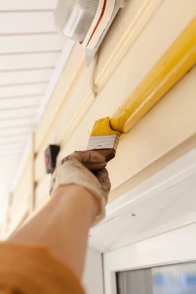 Arbeiter mit Handschuhen färben das Metallgasrohr mit gelber Farbe mit einem Pinsel mit Holzgriff ein. — Stockfoto