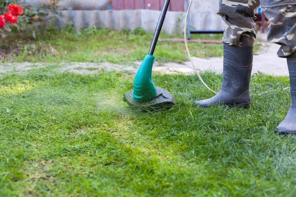 Lastik çizmeler önünde arka bahçesinde bir biçme makinesi ile adam
