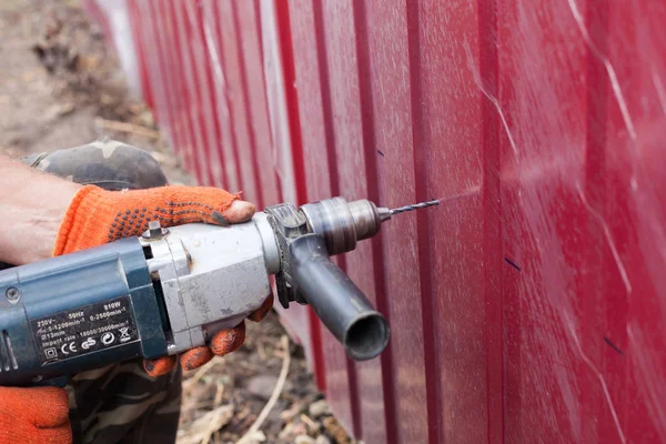 Installation of metal fence. Man drilling a hole in the metal fence.