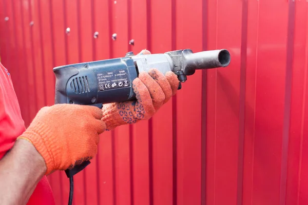 Metal fence installation. Work man in gloves with a drill builds new metal fence.