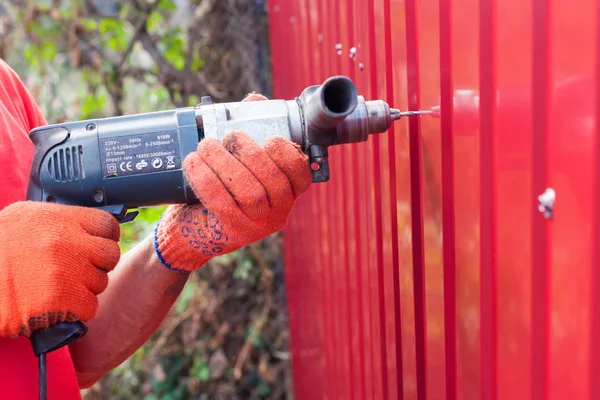 Metal çit yükleme. İş adamı eldiven bir matkap ile yeni metal çit oluşturur. — Stok fotoğraf