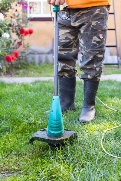 Lastik çizmeler önünde arka bahçesinde bir biçme makinesi ile adam