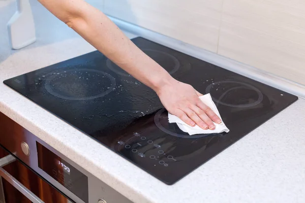 Housewife cleaning and polish electric cooker. Black shiny surface of kitchen top, hands, detergent. — Stock Photo, Image