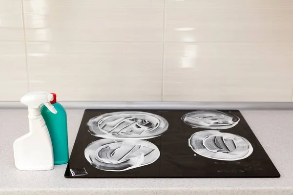 The surface of the induction stove is covered with a detergent. House cleaning - plastic bottles with detergents on kitchen tabletop on the background of electric stoves. — Stock Photo, Image