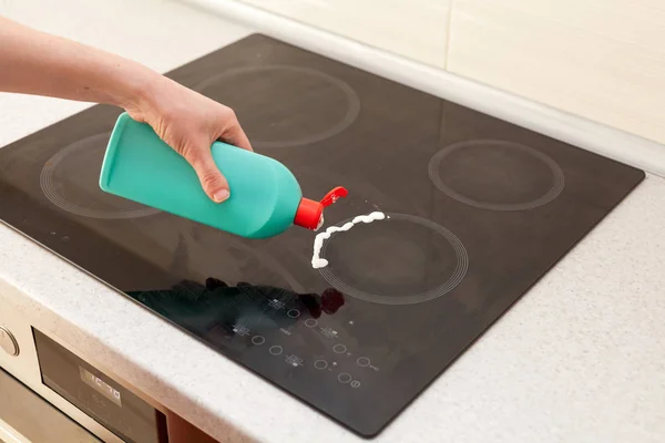 Las manos de mujer con una botella de detergente de limpieza para estufa de inducción aplican un aroma al quemador. Limpieza de la casa — Foto de Stock