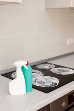 House cleaning - plastic bottles with detergents on kitchen tabletop on the background of electric stoves clipart