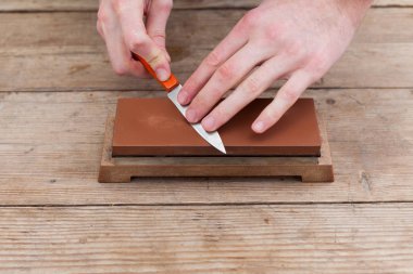 Close up of sharpening the knife with a whetstone on a wooden background. Top view. clipart