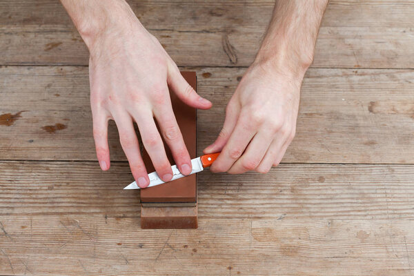 Sharpening the knife with a whetstone on a wooden background. Top view