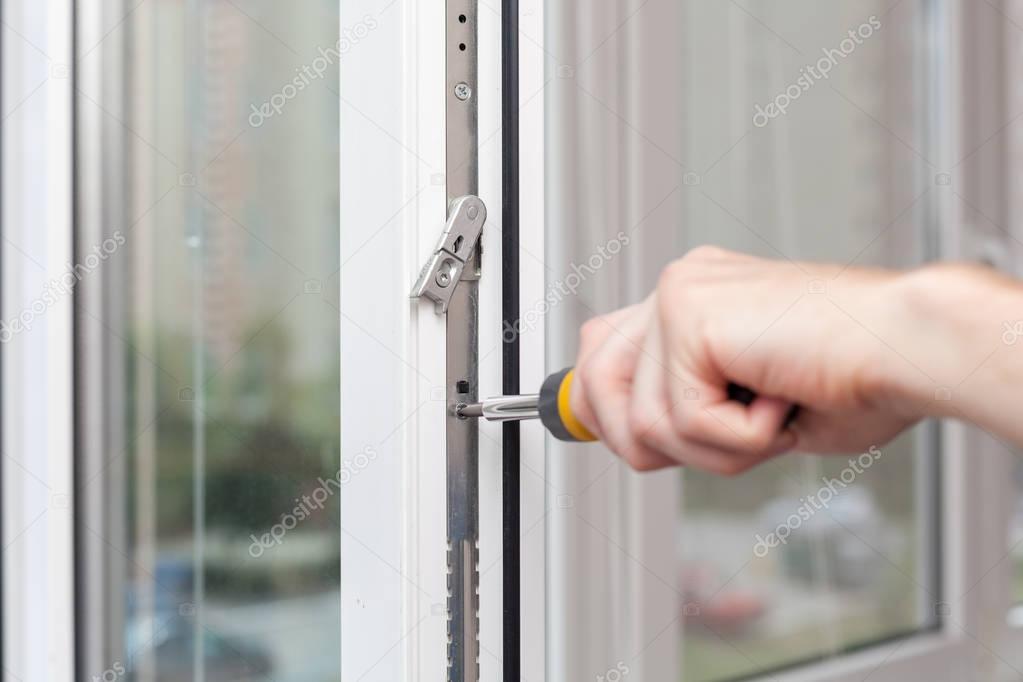 Handyman repairs plastic window with screwdriver.