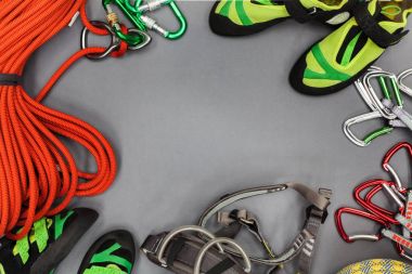 Climbing equipment laid out on on a black background. Rope, climbing shoes, chalk bag, quickdraws, belay, rappel device with carabiner, and other clipart