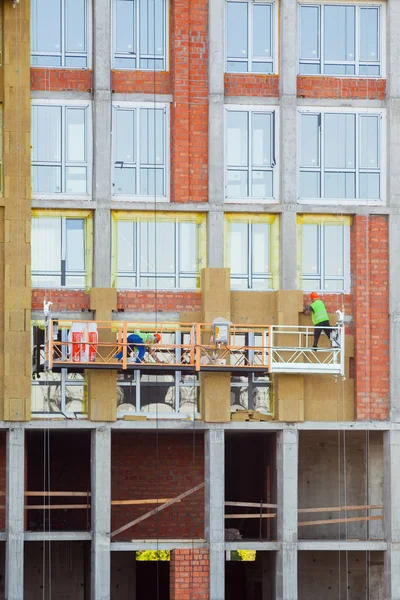 Construction workers insulating house facade with mineral rock wool installation. External wall insulation system (or EWIS) mineral wool for energy saving