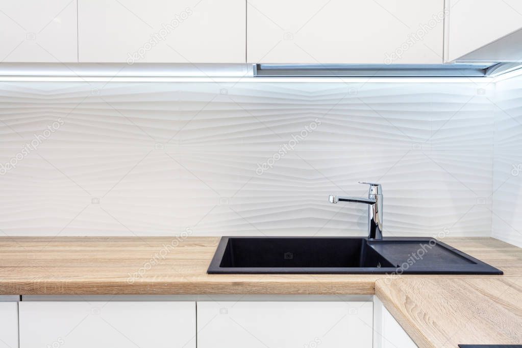 Modern designer chrome water tap over black new kitchen sink. The working area of the kitchen surface is made of wood. Table top made of wood