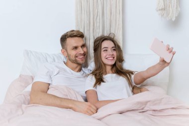 Genç bir kadın ve erkek sabahlarını yatak odasında geçiriyorlar.