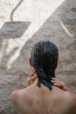 Genç yetişkin kız duş alıyor, banyoda duruyor.