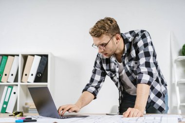 Çalışma odasının planlarıyla çalışan genç bir mimar.