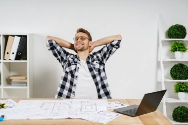 Genç, yetişkin bir mimar. Çalışma odasının planlarıyla çalışıyor.