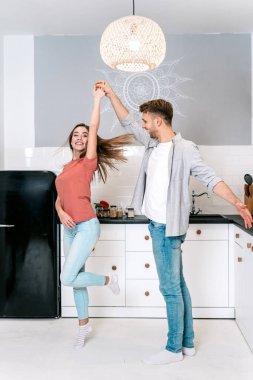 Genç yetişkin karı koca mutfakta dans ediyor.