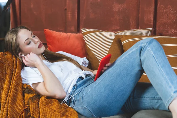 Young adult woman resting at home with smartphone in hands
