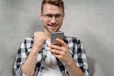 Genç yetişkin bir adam modern akıllı telefon kullanıyor, koltukta oturuyor.