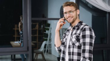 Kendine güvenen genç iş adamının panoramik görüntüsü. Modern akıllı telefonda müşteriyle konuşuyor, mutlu bir yüz ifadesi takınıyor ve gülümsüyor.