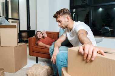 Yorgun ve yorgun genç bir koca yeni bir kiralık eve taşınıyor. Karısı oturma odasında koltukta dinleniyor. Kutu kutuların yanında oturuyor.