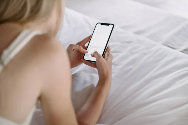 ディスプレイ上のコピースペースと現代のスマートフォンを使用して若い大人の女性の作物ビュー 居心地の良いベッドルームで朝を過ごします ベッドに横たわっています — ストック写真
